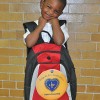 Derrick, a 5-year-old student from the Hawkins St. School smiling as he holds his brand new backpack