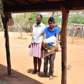 Sobradinho, BA — Dona Idalina  e seu neto levam a cesta de alimentos para casa, que contém arroz, feijão, óleo, açúcar, leite em pó, macarrão, farinha de mandioca e de trigo, fubá, goiabada, gelatina, massa para bolo, extrato de tomate e sal. Itens essenciais e básicos para ajudar no sustento da família.
 

